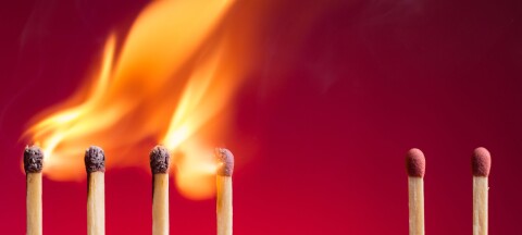 Several matches stand upright on a red background, with one group burning and flames rising above them.
